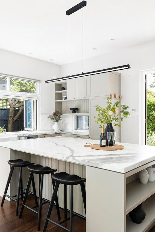 Linear LED pendant light in black above a marble bench top in a kitchen.