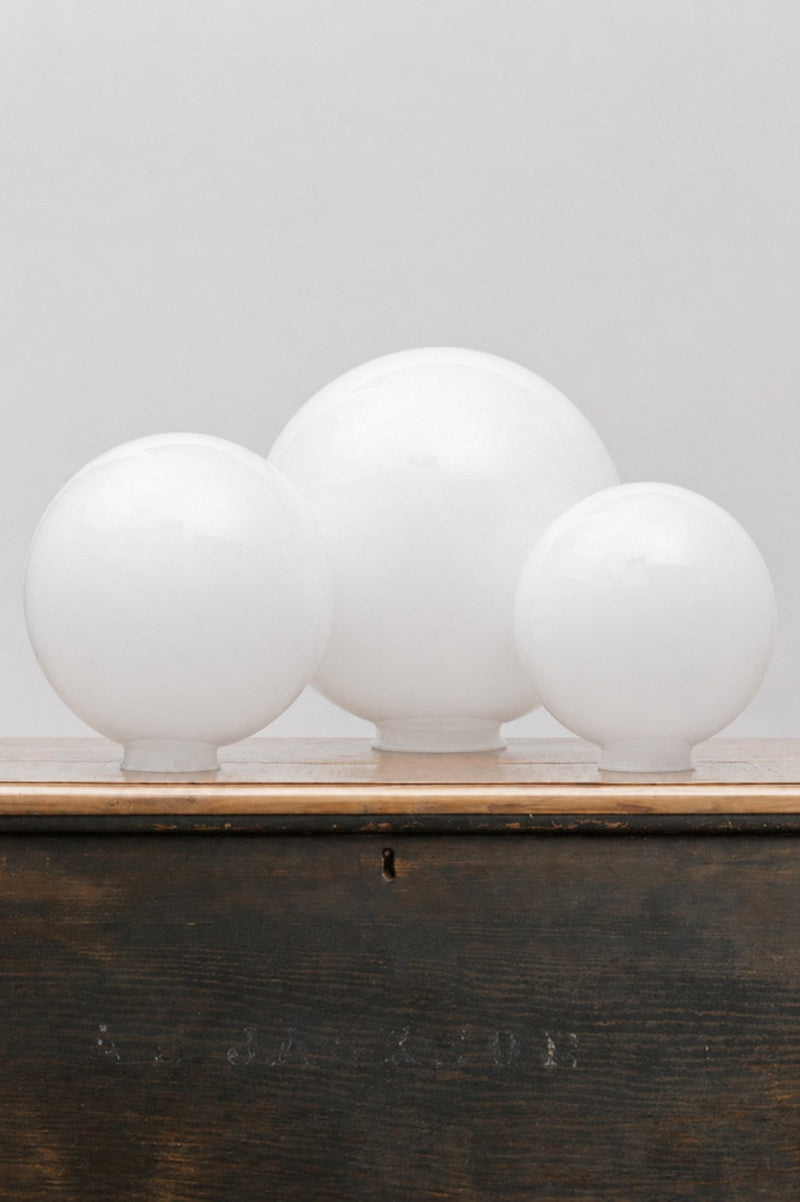 Medium, large and extra large opal glass ball shades sitting on a timber bench. 