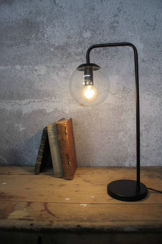 A black metal table lamp with a round clear glass globe shade and a glowing bulb, 