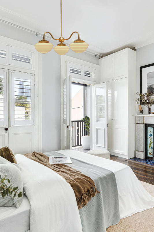 Three light gold/brass gooseneck chandelier with opal shades in a bedroom. 