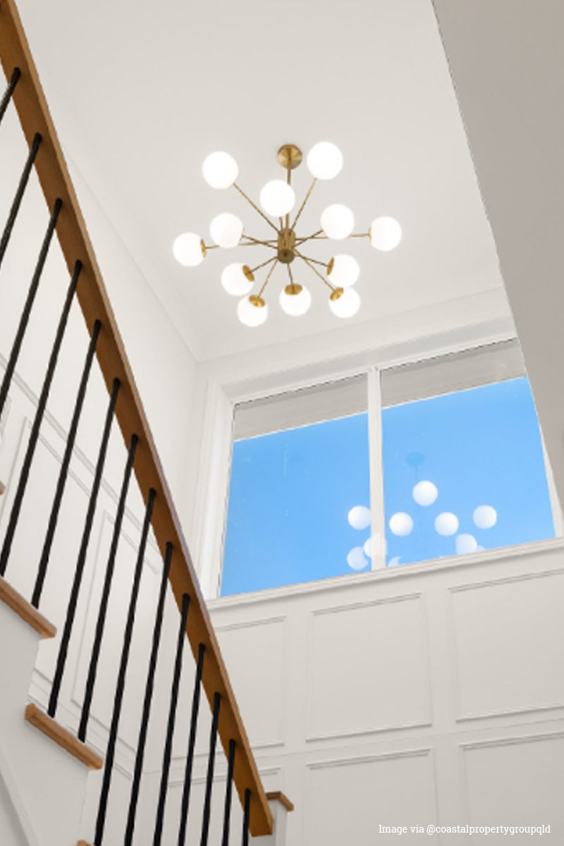 12 light chandelier with opal glass ball shades and a gold fixture n a stairwell void. 