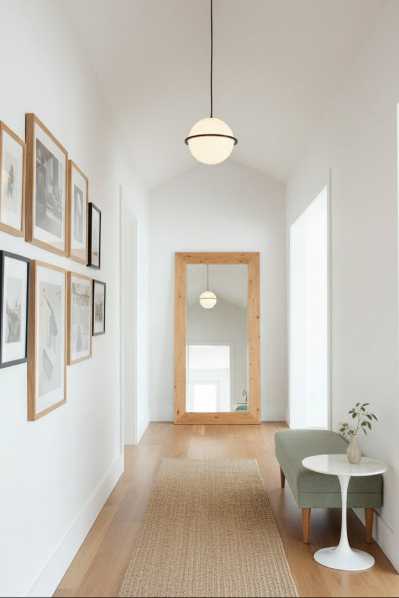 A modern interior hallway with a glass sphere pendant light, light wood flooring, framed wall art.