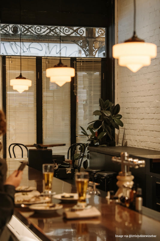 Dining area with tables, chairs, and a plant near a window with decorative ironwork plus our Pensacola Deco Pendant Lights