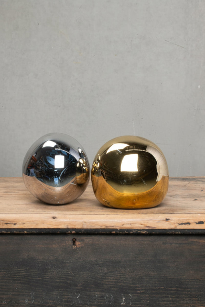Small mirror finished PVC pendant shades in smoke and gols, placed on a timber bench. 