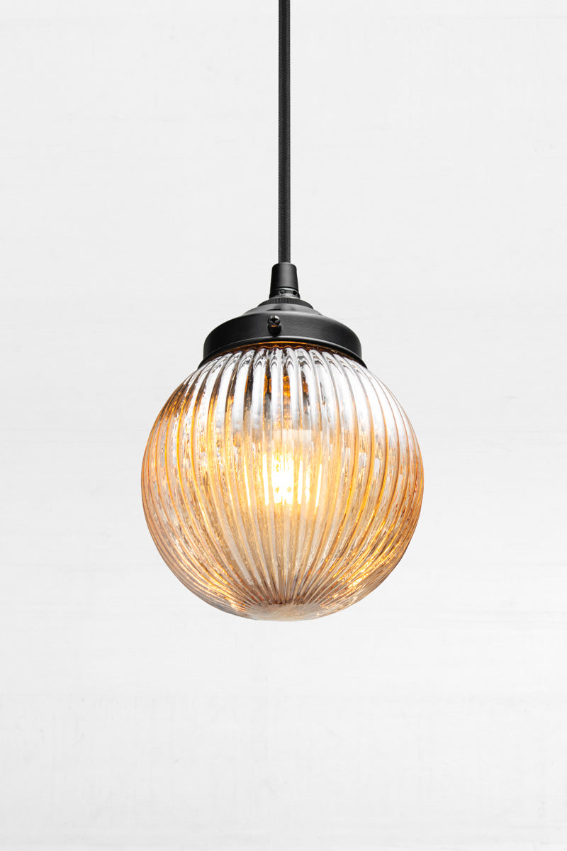 Dark Amber reeded glass ball shade on a black pendent cord with black metalware. 