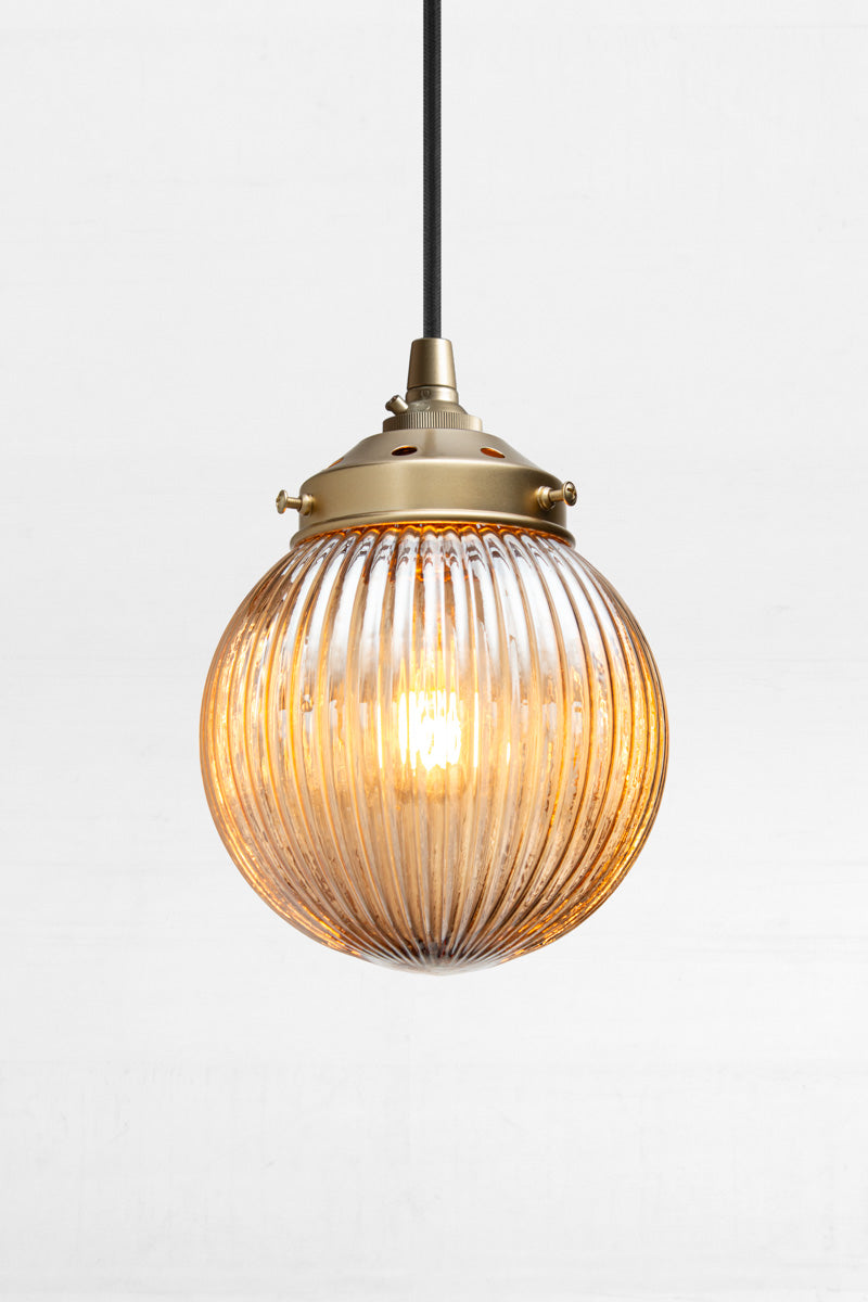 Dark Amber reeded glass ball shade on a black pendent cord with gold/brass metalware. 