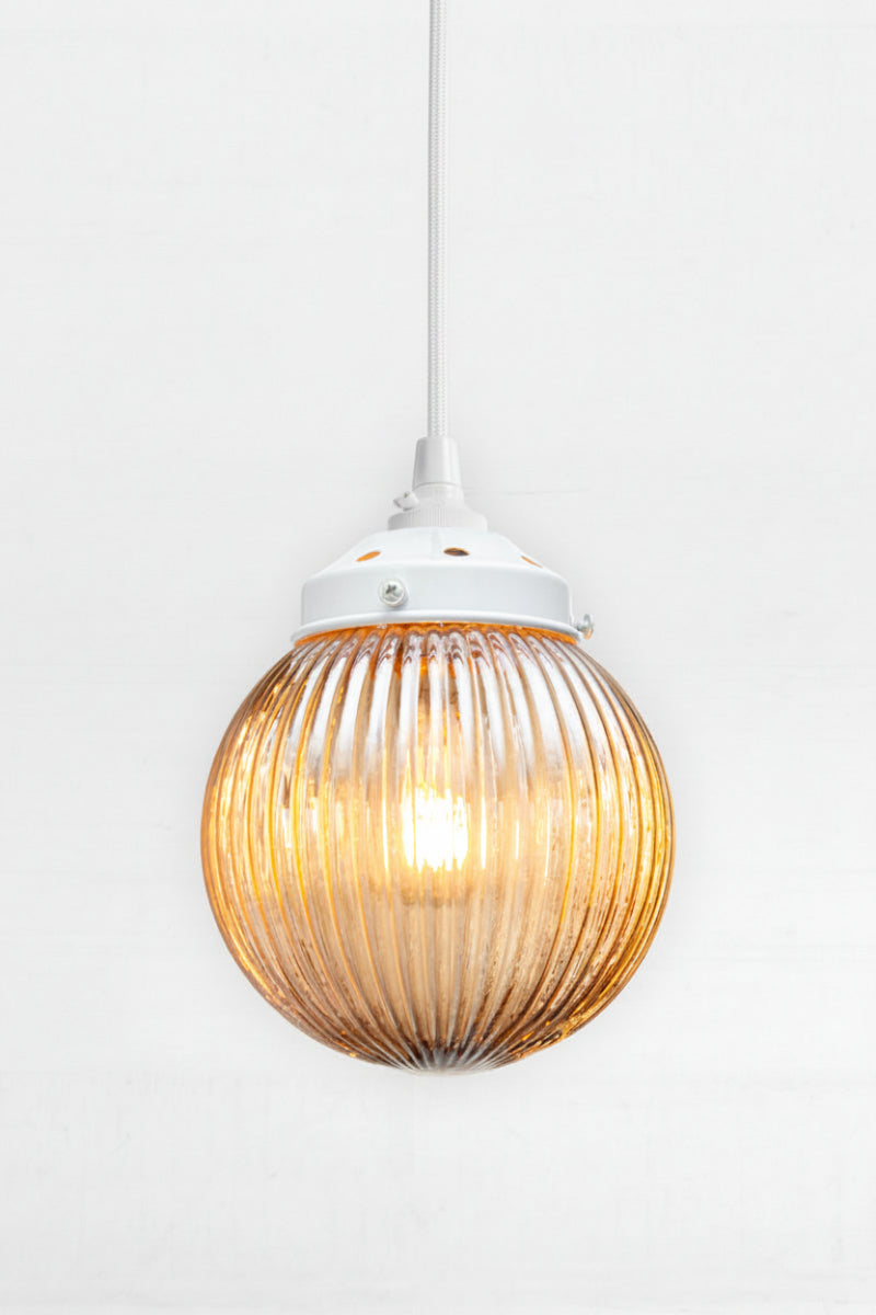 Dark Amber reeded glass ball shade on a white pendent cord and metalware. 
