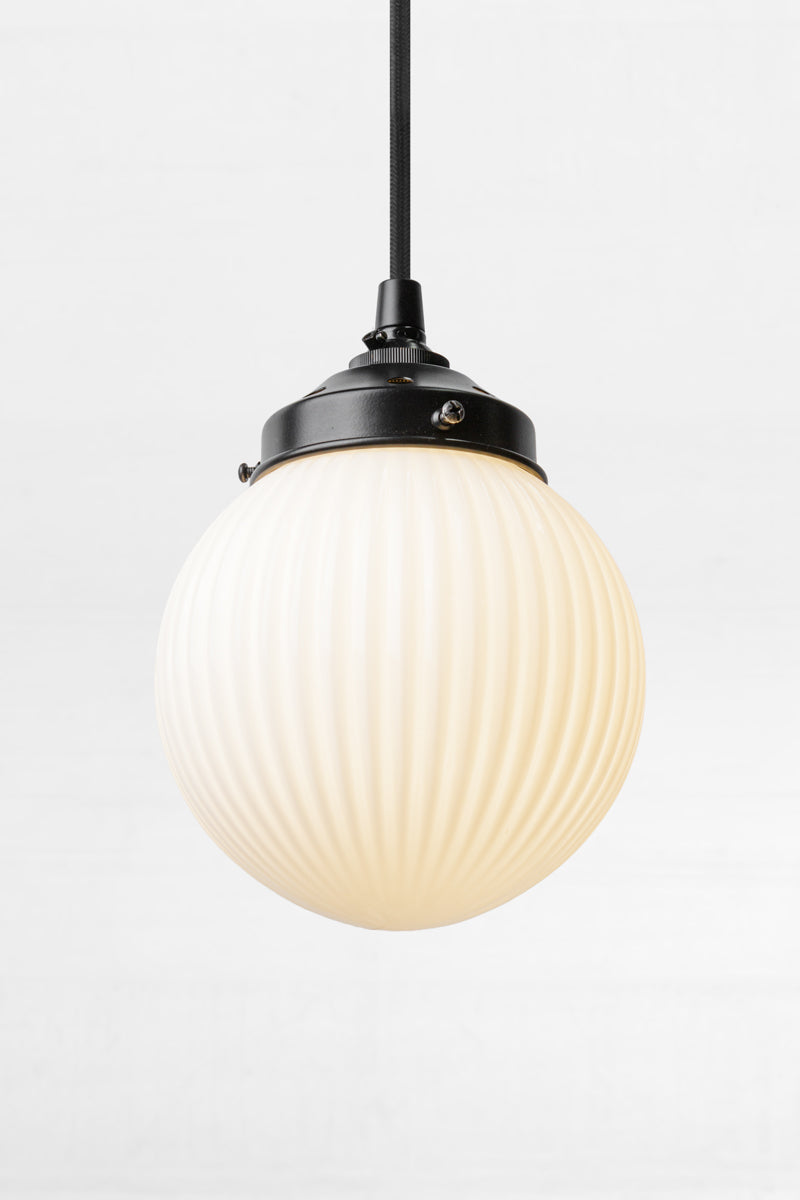 Glass ball shade in opal with vertical reeded detailing on a black pendant cord. 