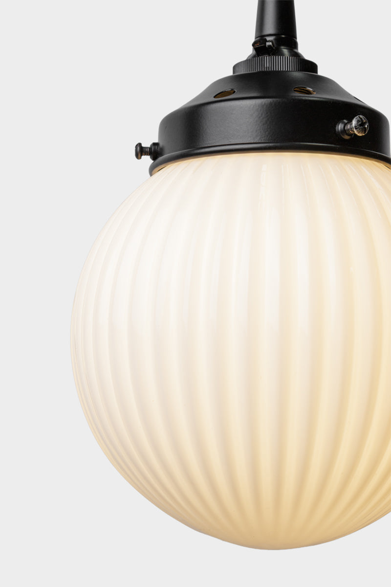 Close up of the opal glass ball shade with vertical reeded detailing on a black pendant cord. 