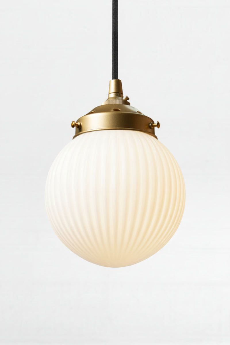 Opal glass ball shade with reeded detailing on a black pendant cord with  a gold/brass gallery. 