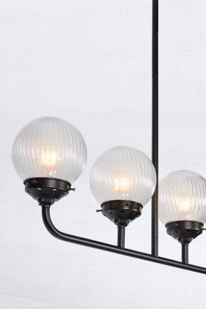 Close up of the Black five lamp linear chandelier with clear reeded glass ball shades. 