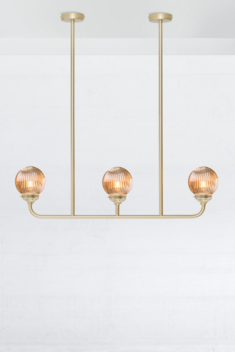 Gold/brass triple lamp linear chandelier with dark amber reeded glass ball shades. 