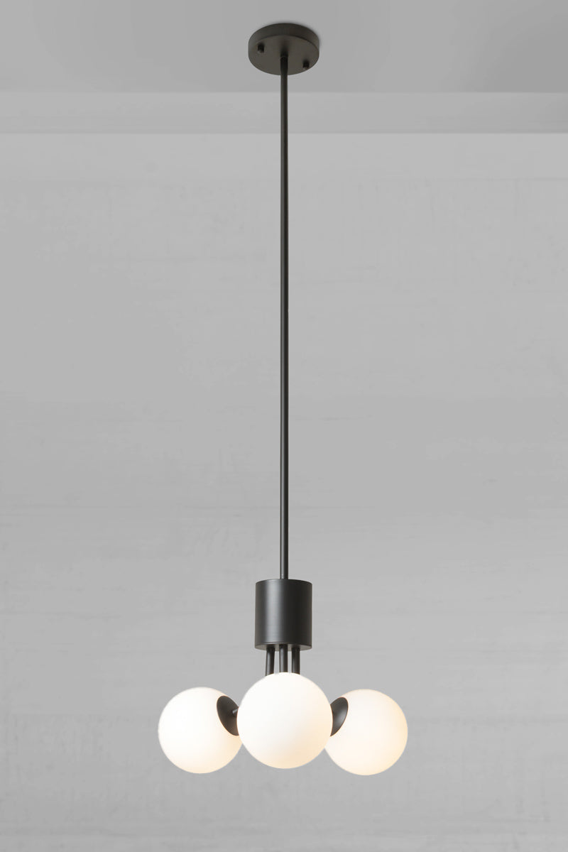 Brooklyn Glass Orb 3 Light Pendant is a modern three-light pendant chandelier with a matte black metal frame and spherical opal glass shades, suspended from a ceiling against a light gray wall.