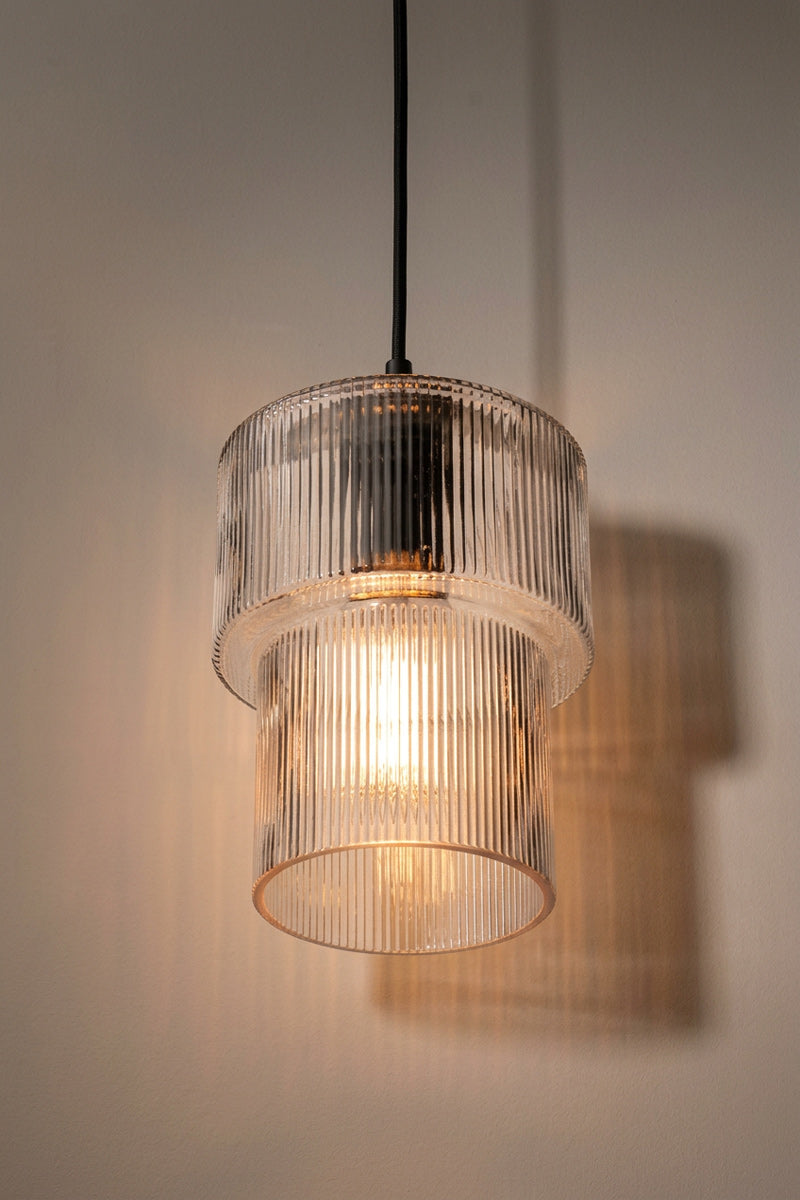 A modern pendant light with a dual-tiered, ribbed clear glass shade, suspended by a black cord 
