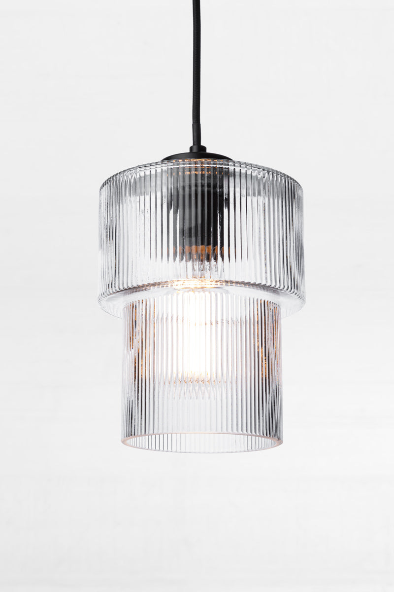 Art deco inspired glass shade in clear with reeded detailing and a tiered form with a black pendant cord. 