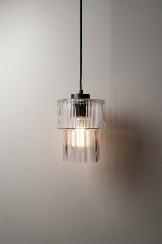 A glass pendant light with a ribbed clear glass shade and a black suspenion cord a