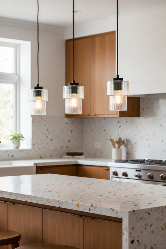 Three clear reeded glass tiered shades on black cords in a light filled kitchen featuring timber and terrrazzo. 
