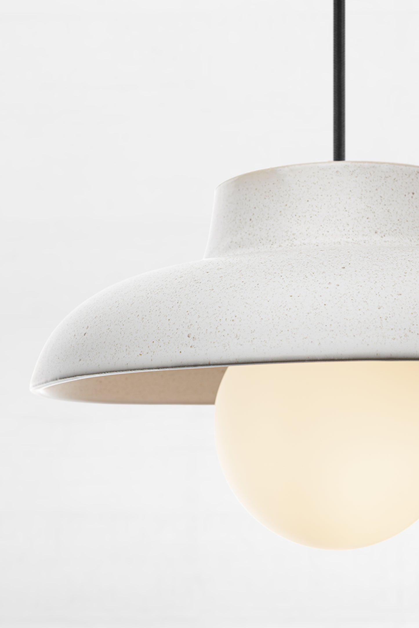 Close up of the ceramic light grey pendant light with opal glass ball shade and black fabric cord. 