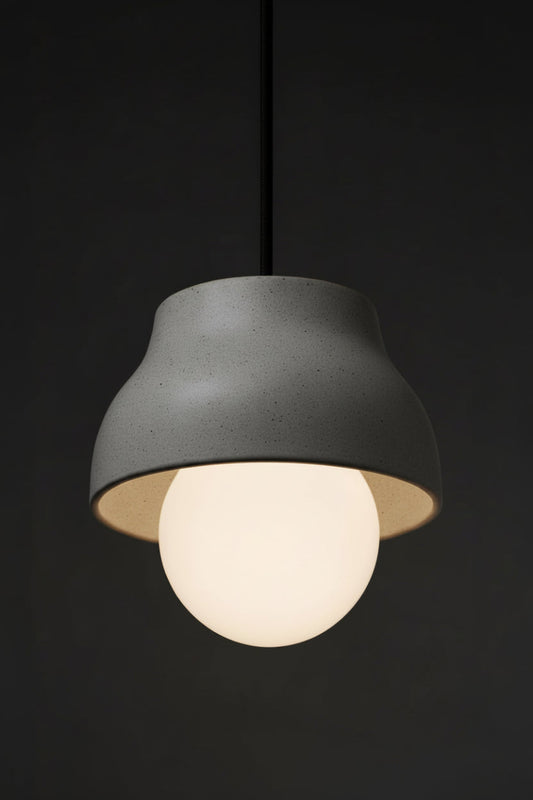 Small ceramic light grey pendant light with opal glass ball shade and black fabric cord in a darkend room. 