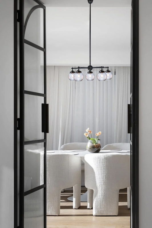 Black five arm Chandelier with clear reeded glass ball shades, over a modern dining space. 
