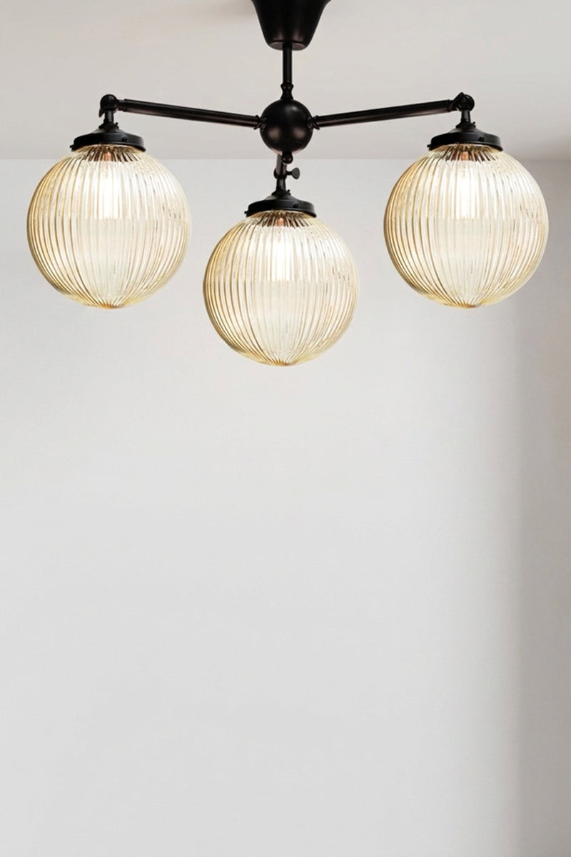 Three arm flush mount light in black with medium amber, reeded, glass ball shades. 