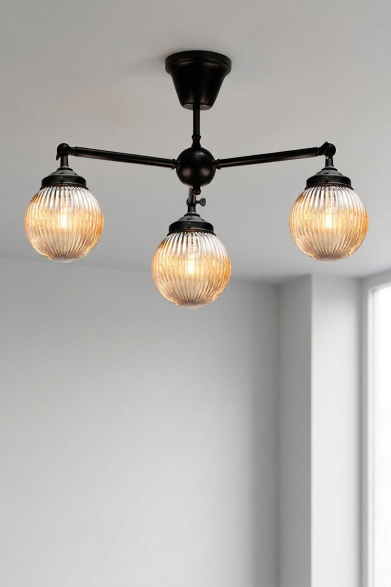 Three arm flush mount light in black with dark amber, reeded, glass ball shades. 
