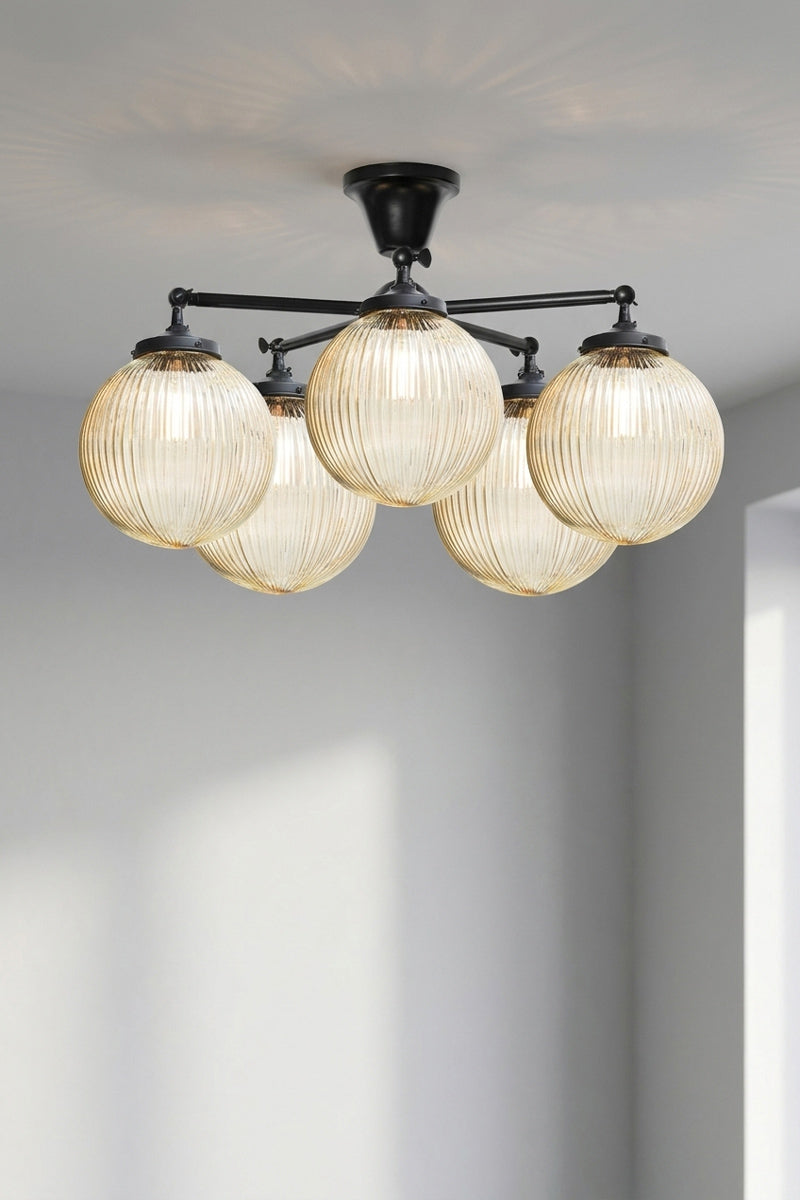 Five arm flush mount light in black with medium amber, reeded, glass ball shades. 