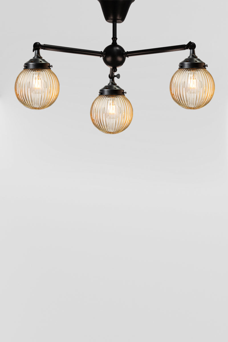 Three arm flush mount light in black with amber, reeded, glass ball shades. 