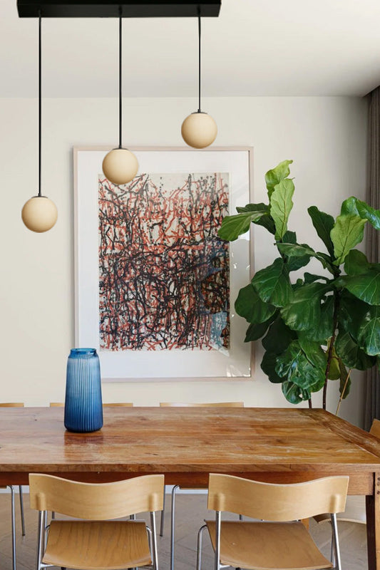 Three drop linear light with black cords and amber glass ball shades. 