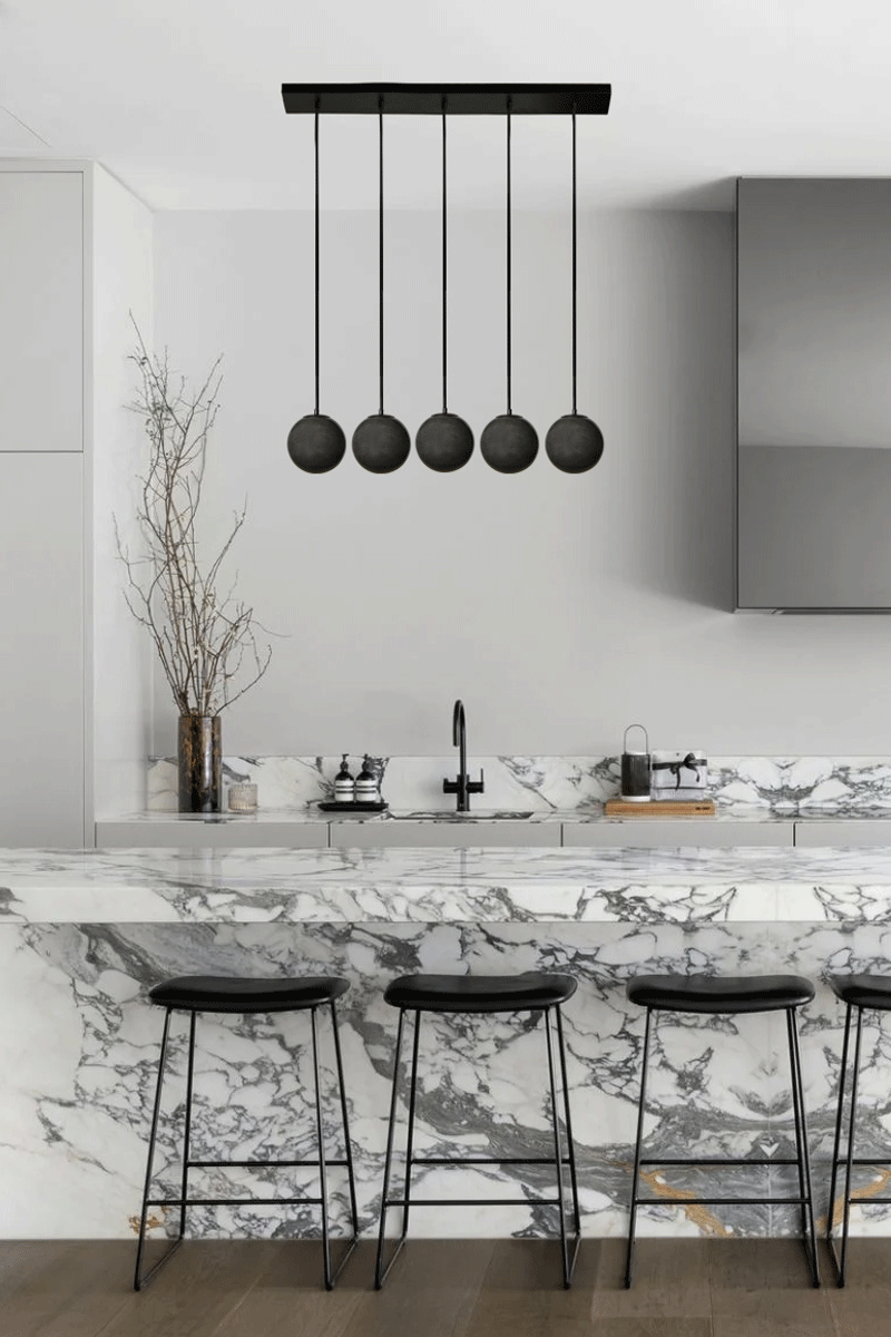 Five drop linear light with black cords and dark grey glass ball shades. 