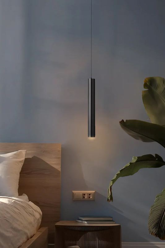 Gunmetal coloured LED slimline pendant light as a bedside light in a moody room with greenery. 