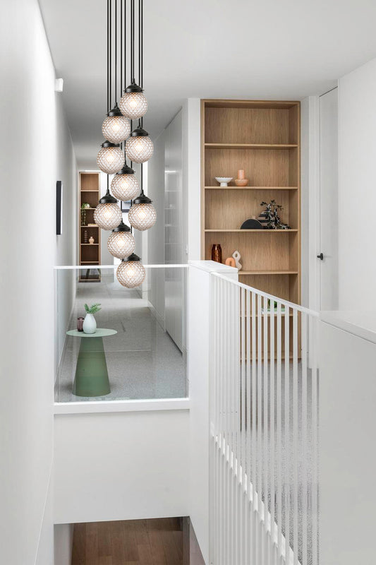 9 drop chandelier with vintage inspired glass shades on a black fixture over a stairwell. 