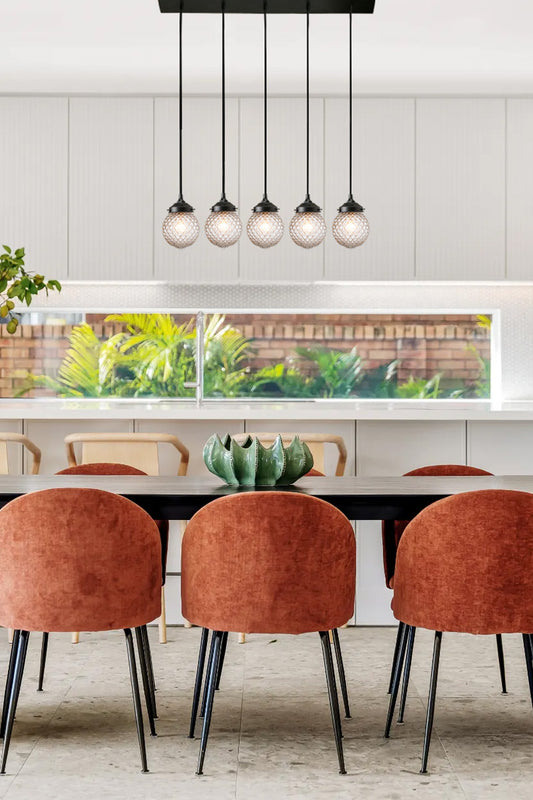 Five light multi drop pendant on a linear ceiling mount in black with clear glass shades a dining space. 