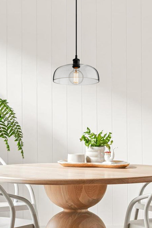 Clear glass shade with black hardware over a dining space. 