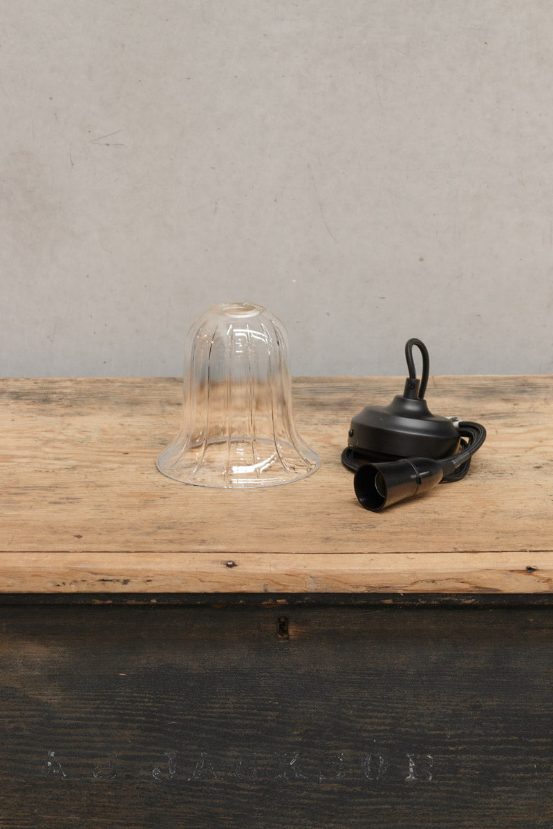 Uninstalled clear glass bell shade and black pendant cord