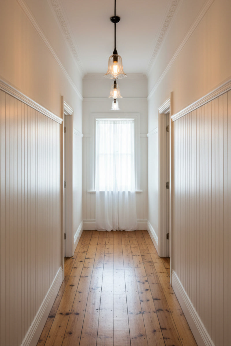 Long hallway with wooden floor and white pannel walls, featuring bell shaped pendant lights.