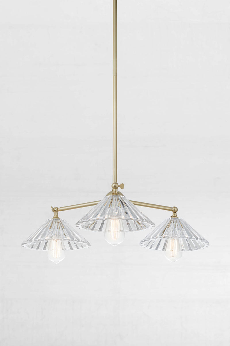 Angled view of the Gold/ Brass three light pendant with tiltable lampholders and three pleated glass shades. 