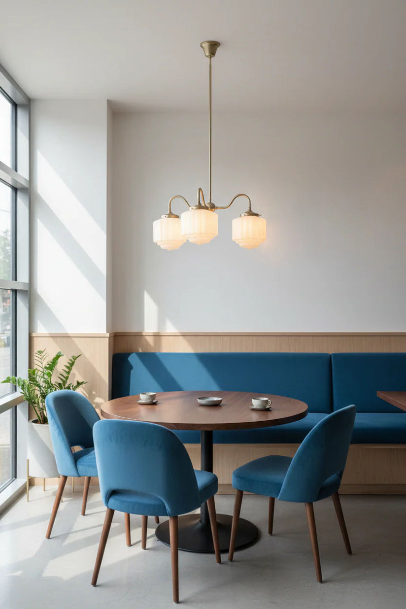 Deco 3 arm light in modern interior with blue upholstered chairs and a round wooden table near a large window.
