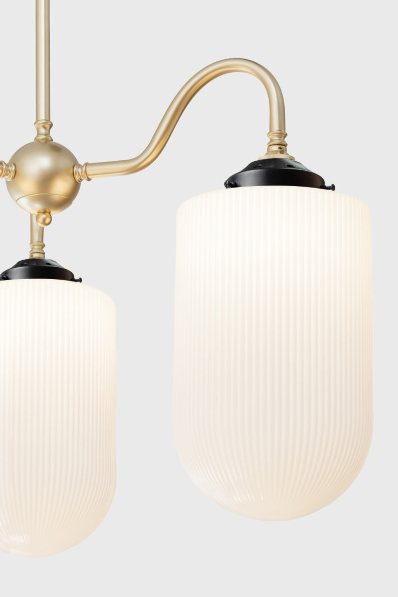 Close up of the large reeded opal glass shades on the gold/brass triple arm gooseneck chandelier with black galleries. 