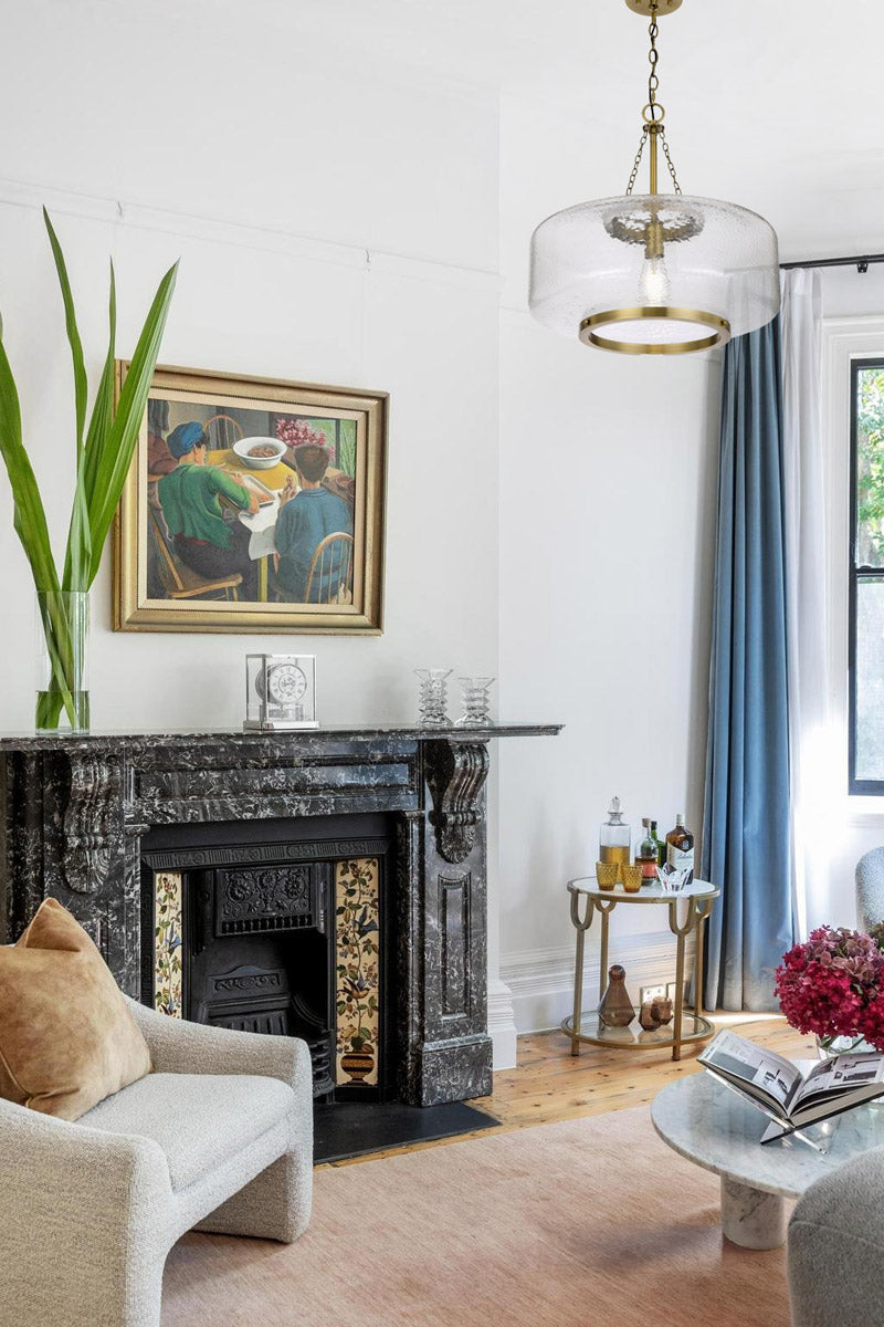 Gold/brass oval shade pendant light with textured glass.  in a bright sitting room with a marble fireplace.