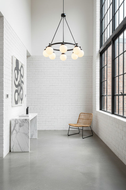 8 light black, circular chandelier with opal glass ball shades installed in a white industrial styled loft hallway. 