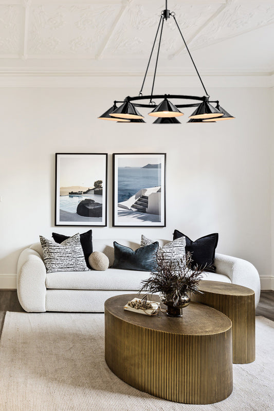 Living room with a round gold table, featuring a modern chandelier with eight black cone shades. 