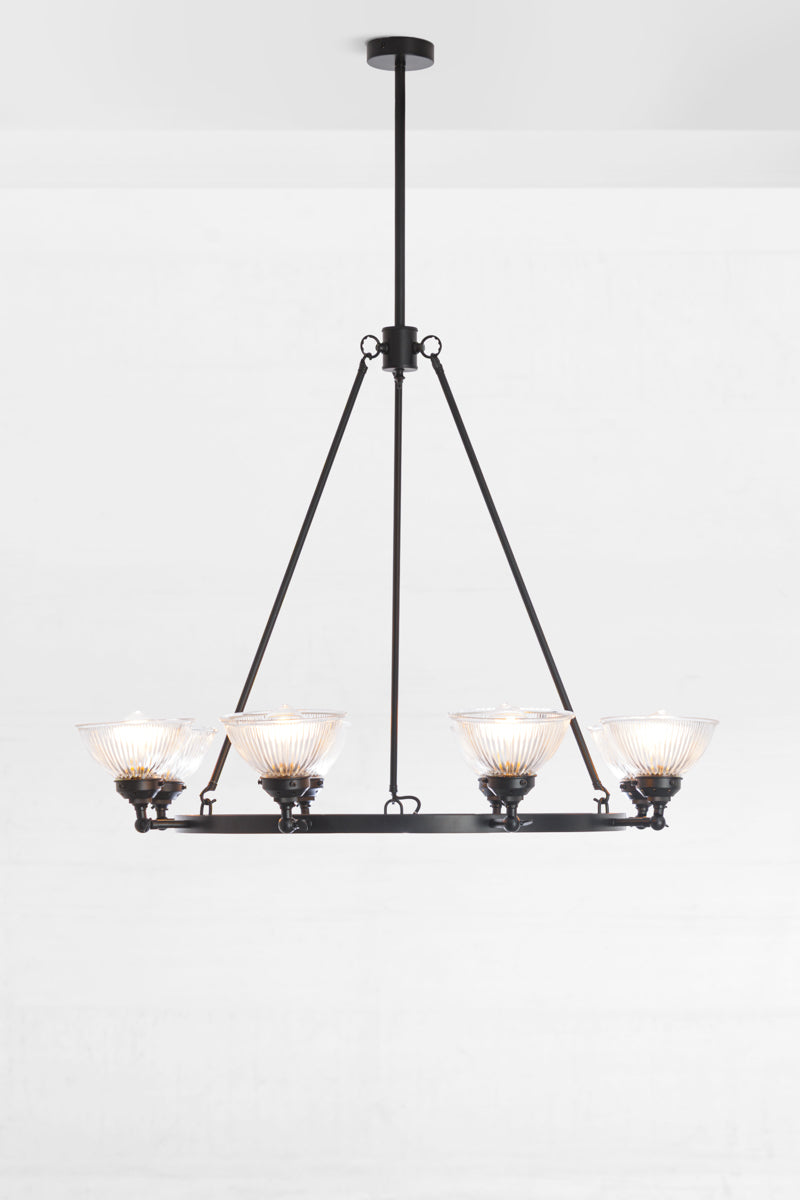 Matt black circular chandelier featuring 8 clear glass ridged shades with the lampholders facing up. 