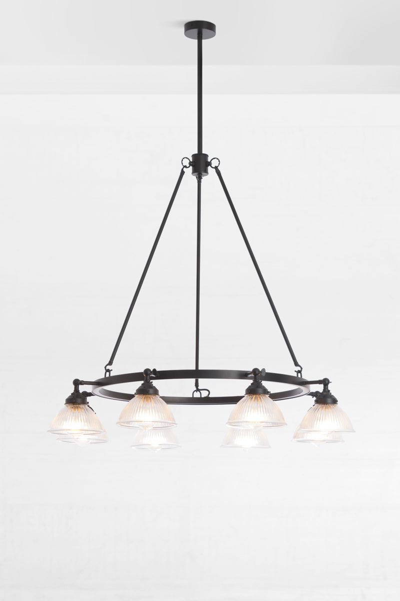 Matt black circular chandelier featuring 8 clear glass ridged shades with the lampholders facing down. 