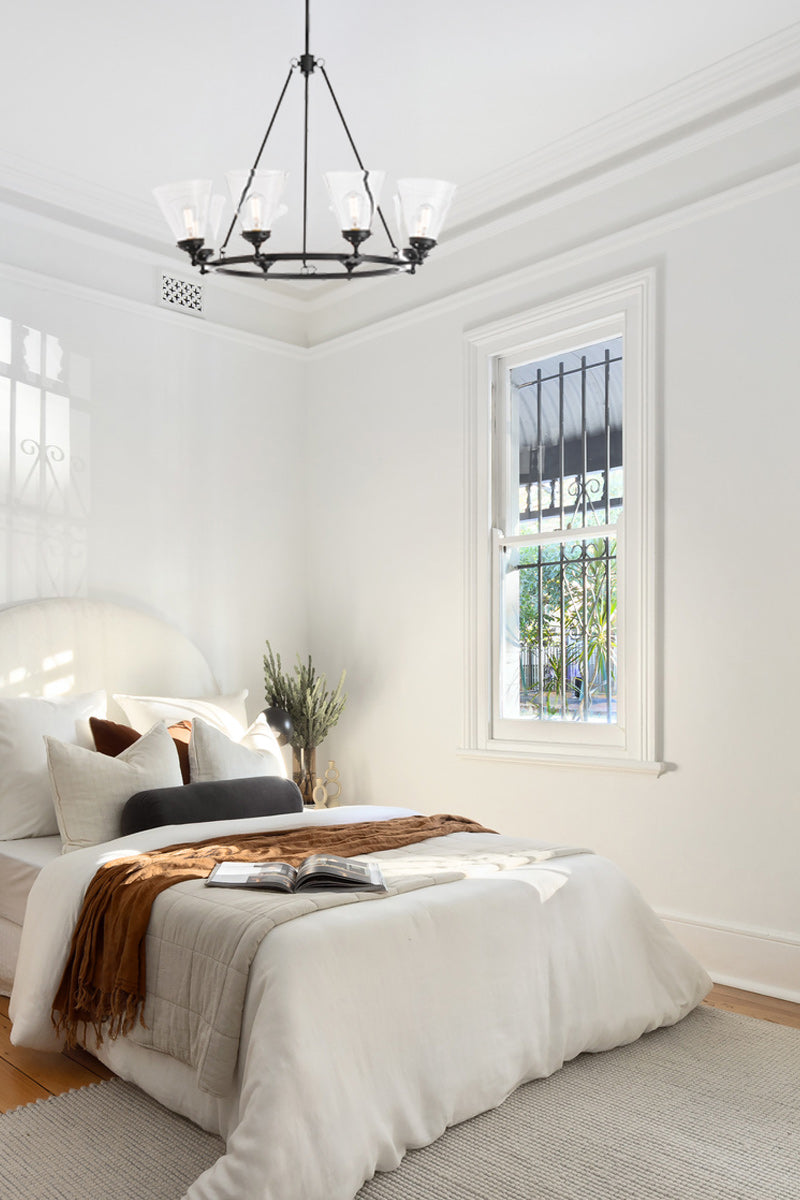 Eight light circular chandelier in black with clear glass shades in bright white bedroom. 