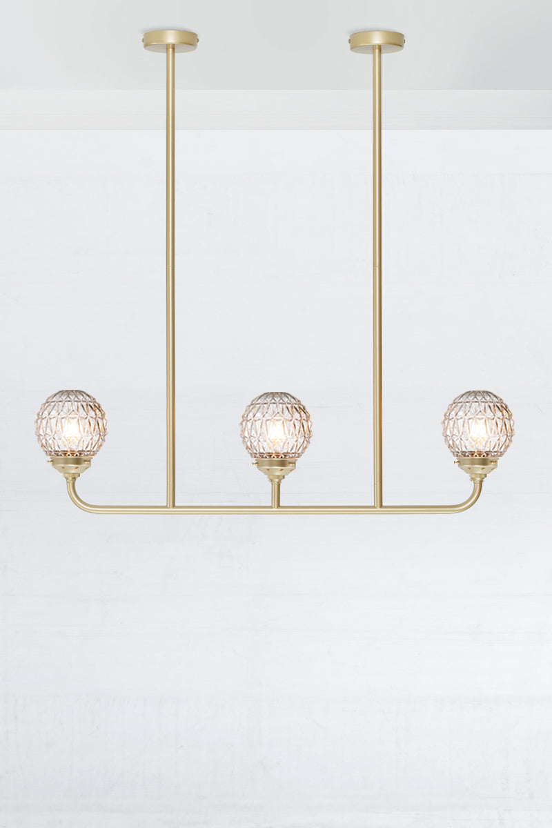 Three light linear chandelier in gold/brass with clear glass ball shades with a Geometric pattern.