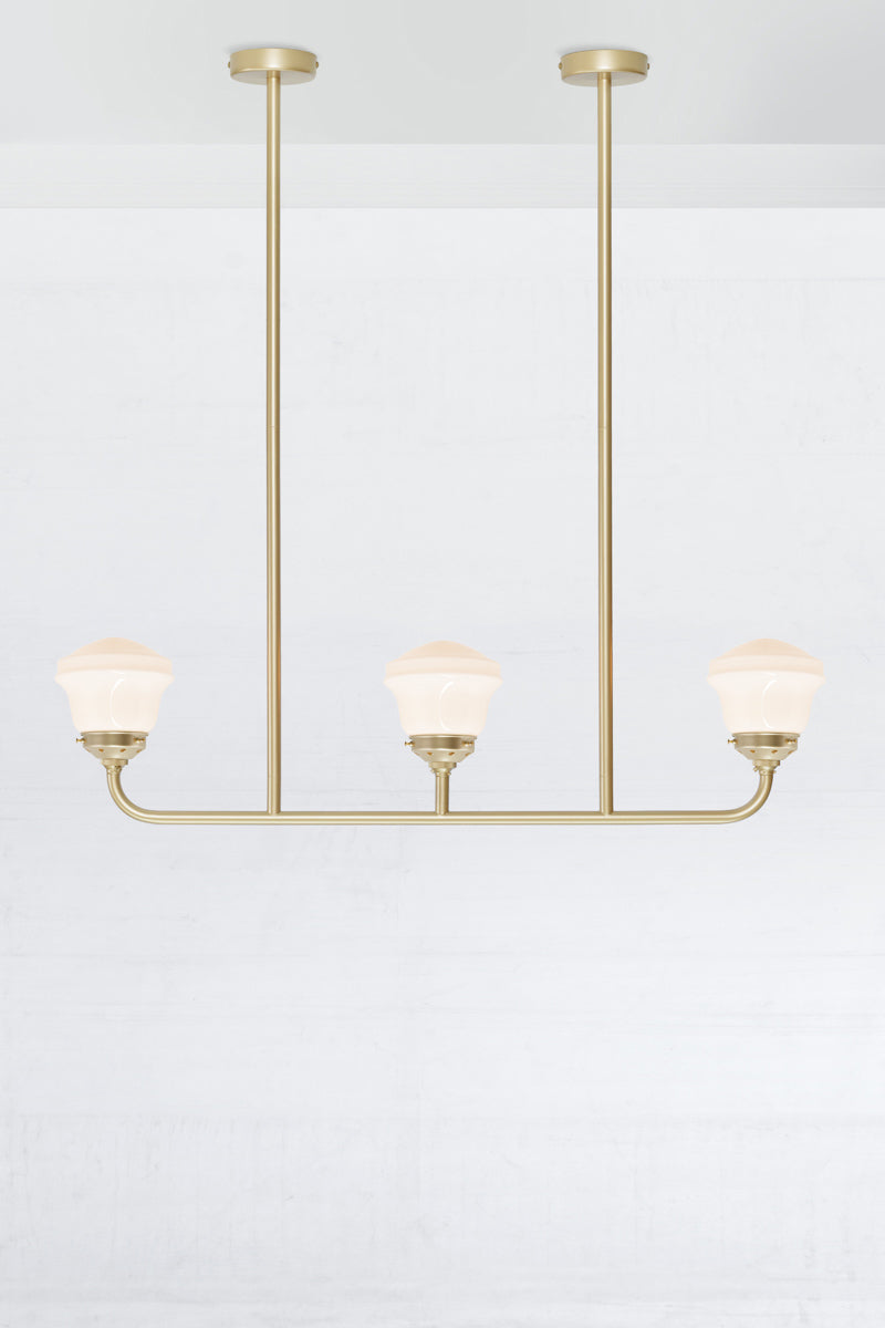 Gold/brass 3 light linear chandelier with gold/brass galleries and opal schoolhose shades. 