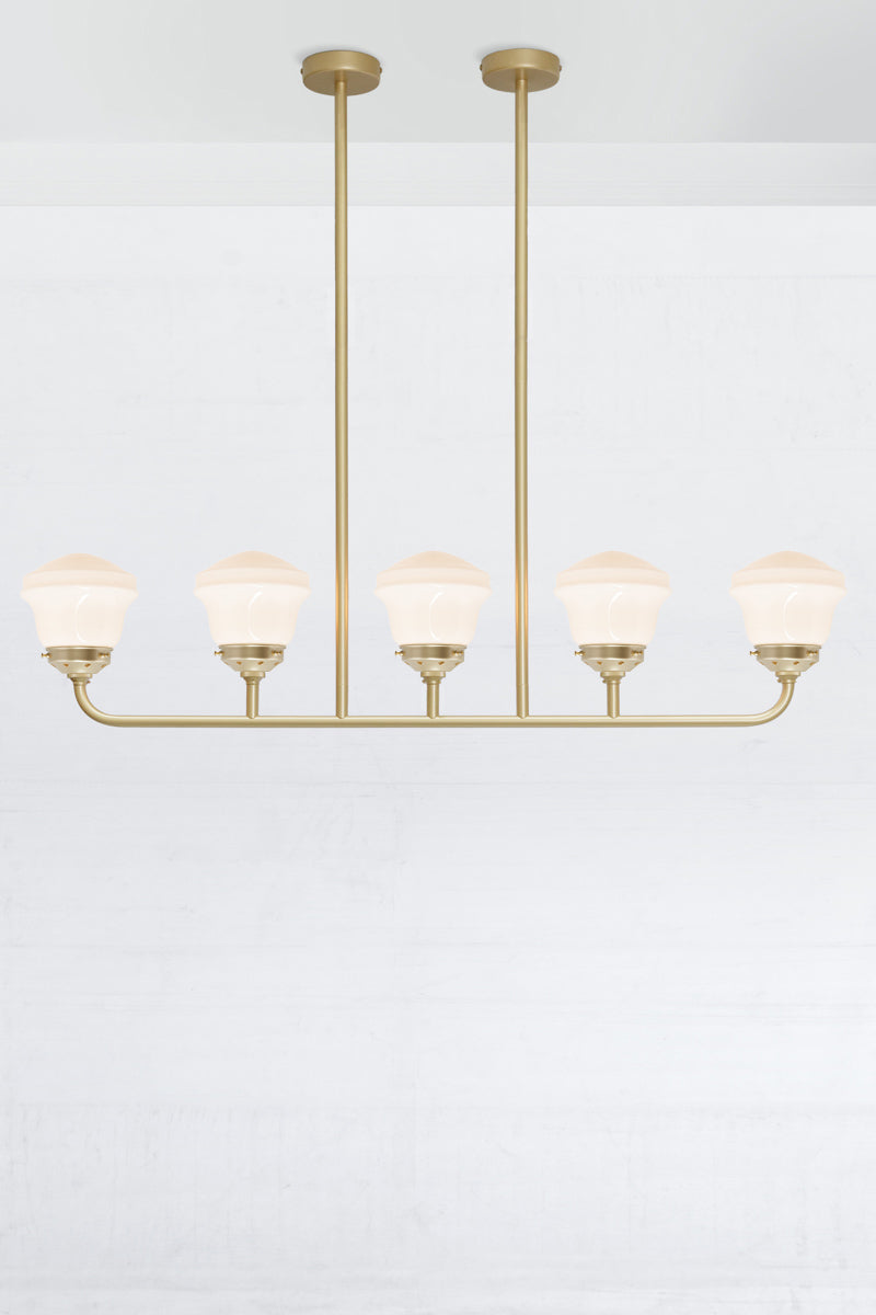 Gold/brass 5 light linear chandelier with gold/brass galleries and opal schoolhose shades. 