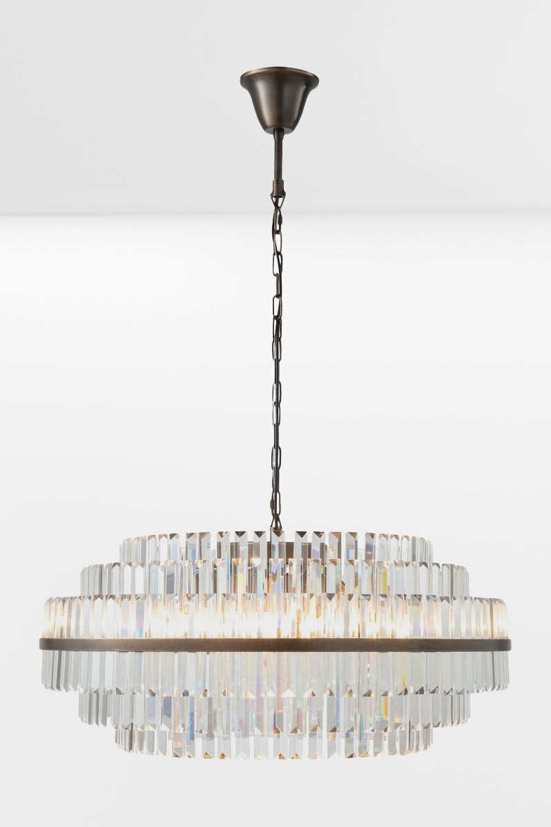 Large glass chandelier with antique brass metalwear and three tiers with the lights on. 