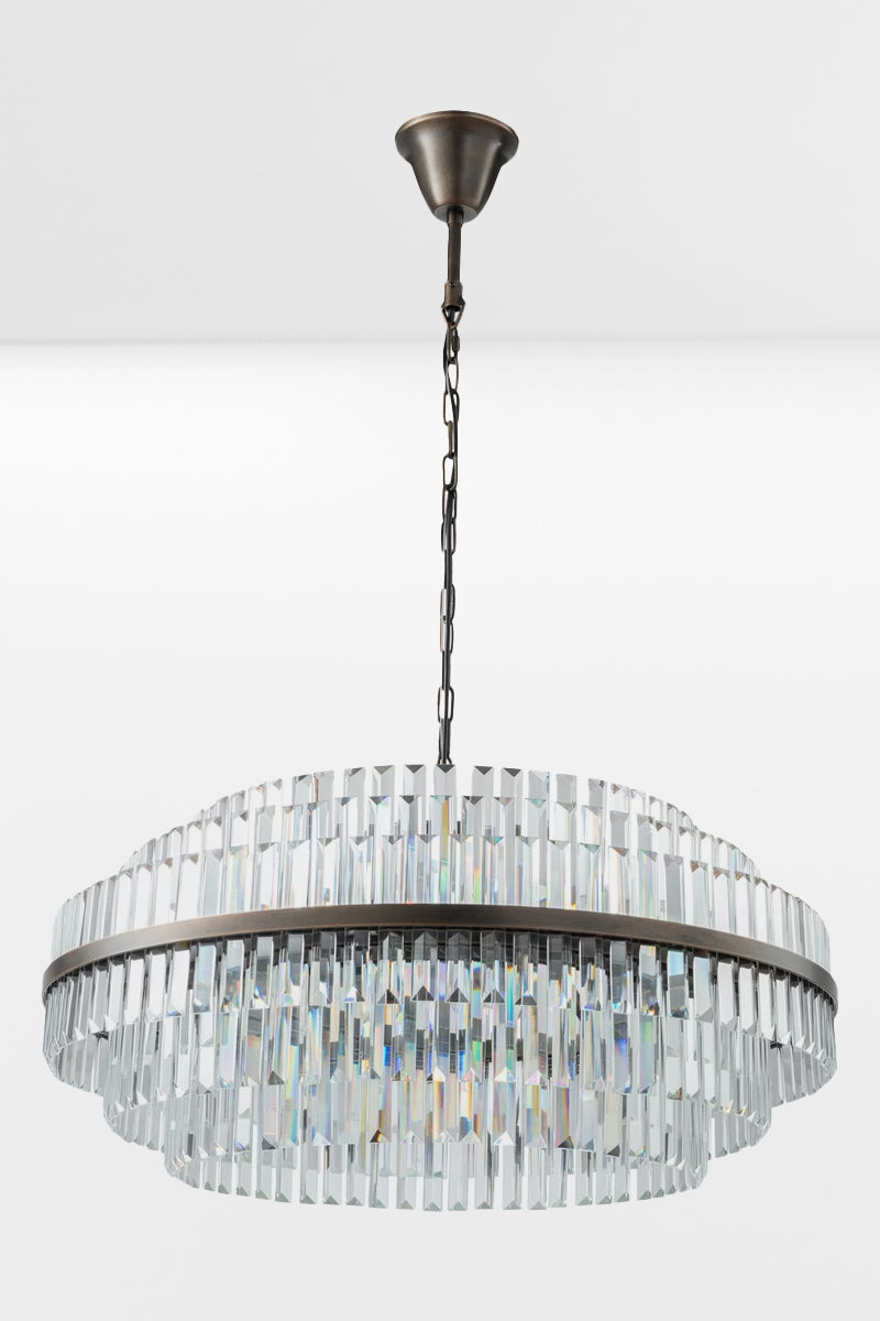 Large glass chandelier with antique brass metalwear and three tiers with the lights off.